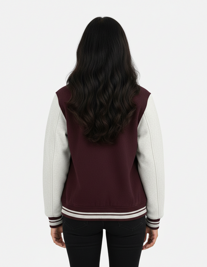 Woman with long wavy black hair wearing maroon and white varsity jacket and black jeans, back view