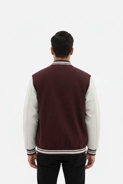Man wearing maroon and light gray varsity jacket standing with back to camera on white background