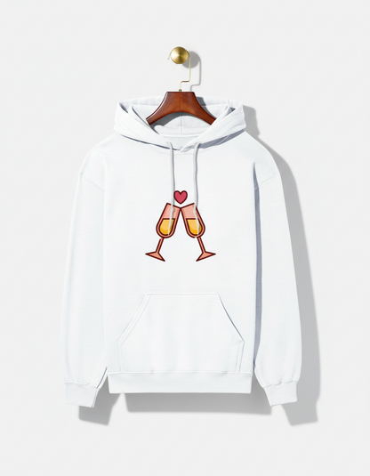 White hoodie with clinking champagne glasses and heart graphic on front, hanging on wooden hanger