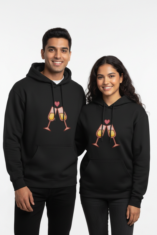 Smiling young man and woman wearing matching black hoodies with clinking champagne glasses and heart graphic