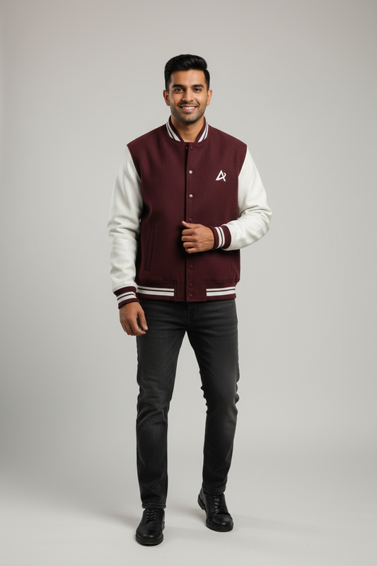 Smiling man wearing maroon and white varsity jacket with logo, black jeans, and black shoes