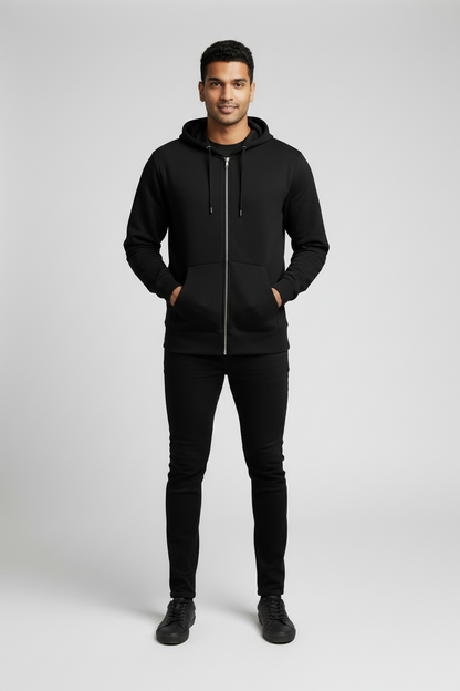 Smiling man wearing black zip-up hoodie, black pants, and black sneakers on gray background