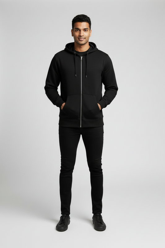 Smiling man wearing black zip-up hoodie, black pants, and black sneakers on gray background